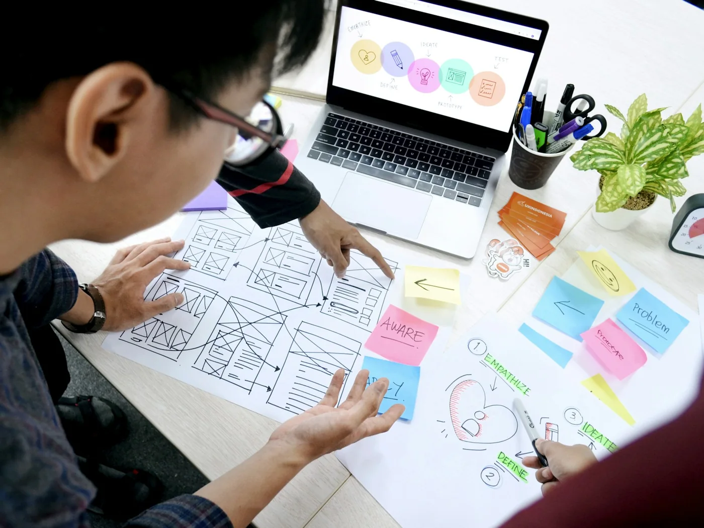 People planning paper website wireframes beside a laptop on a white desk